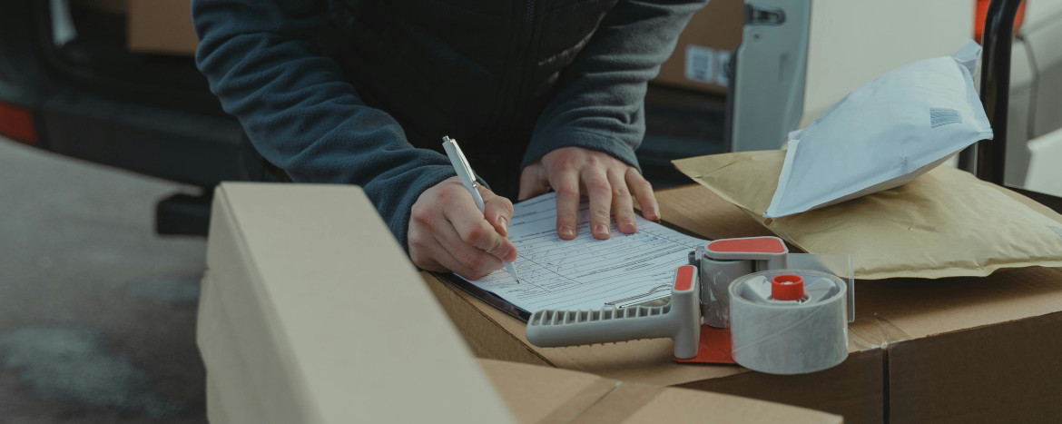 Closeup of a delivery person's hands signing a document on a table full of boxes.